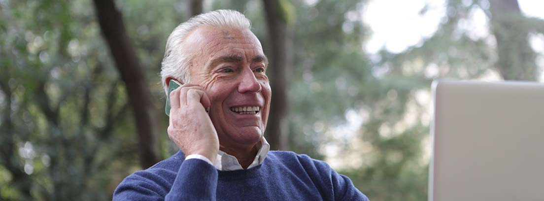Hombre mayor sonriente usando un ordenador y un teléfono móvil