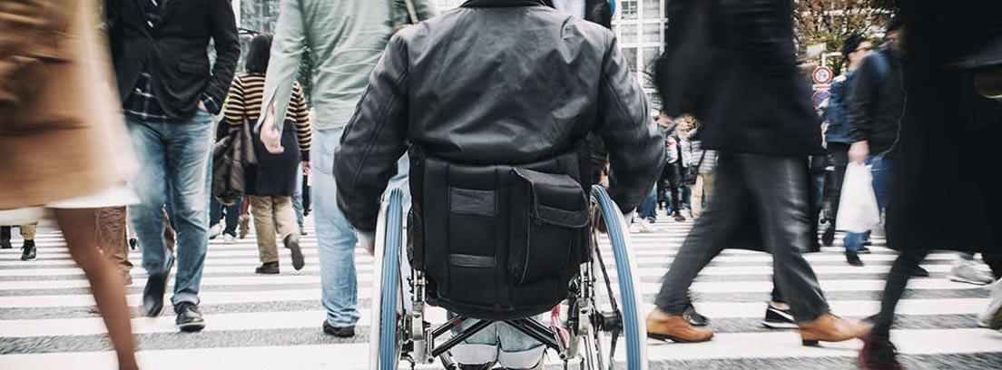 Hombre de espaldas en una silla de ruedas cruzando un paso de peatones