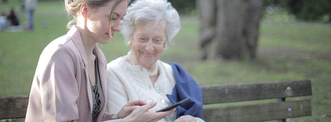 Anciana con mujer joven mirando un smartphone