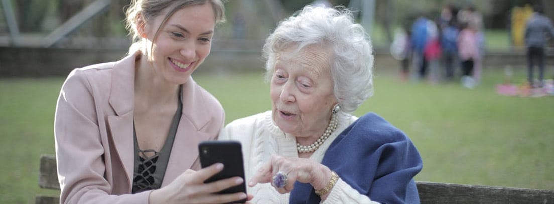 Una anciana observa la pantalla de un smartphone que le enseña una mujer joven