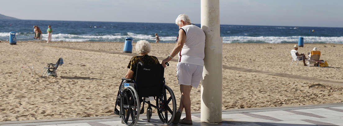 Señal con fondo azul y silla de ruedas junto a pasarela de madera en playa.