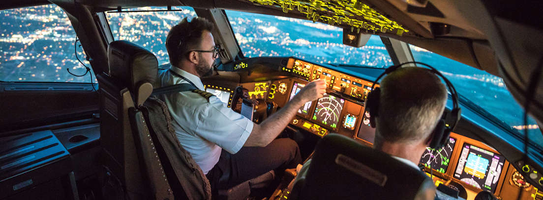 Dos personas de espaldas delante de un cuadro de mandos de un avión
