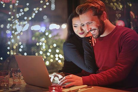 Hombre sonriente con manos sobre teclado de portátil y mujer apoyada en su hombro