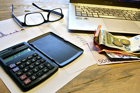Calculadora sobre papeles y junto a gafas, dinero en euros y ordenador