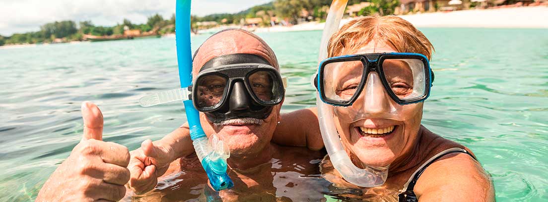 Una parejas de jubilados ataviados con su equipo de snorkel se realizan un selfie dentro del agua