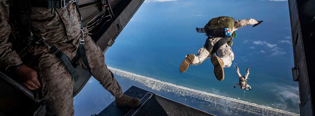 Persona con traje militar mira como otros con paracaidas flotan en el aire