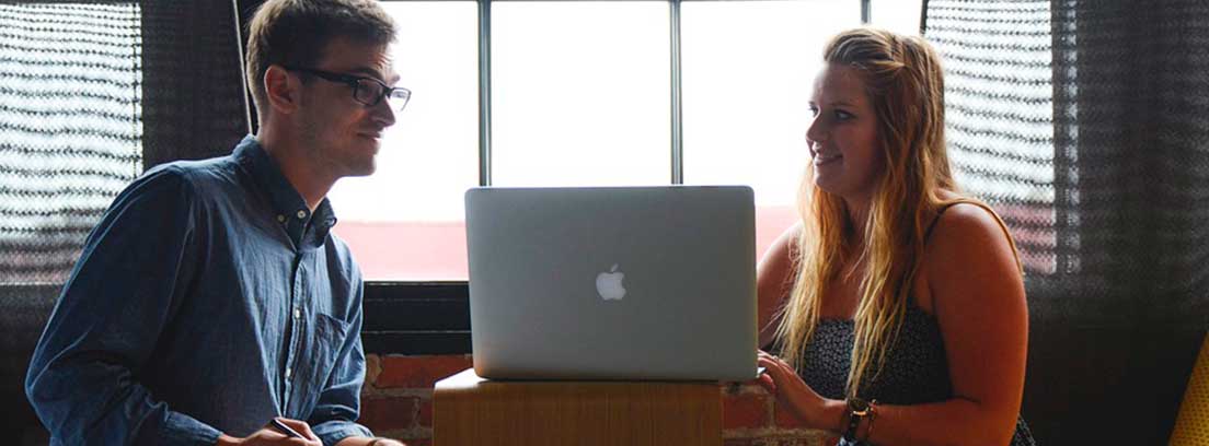 Hombre y mujer sentados una a cada lado de una mesa con ordenador portátil entre ellos
