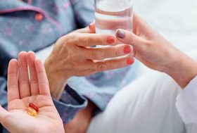 Mujer con un vaso de agua y dos pastillas en la mano