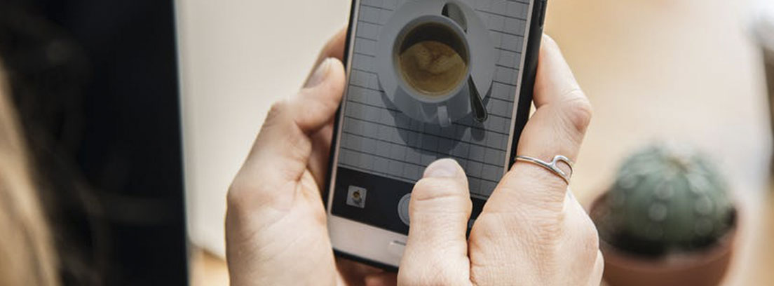 Manos sujetan un Smartphone en el que se ve una taza blanca con café