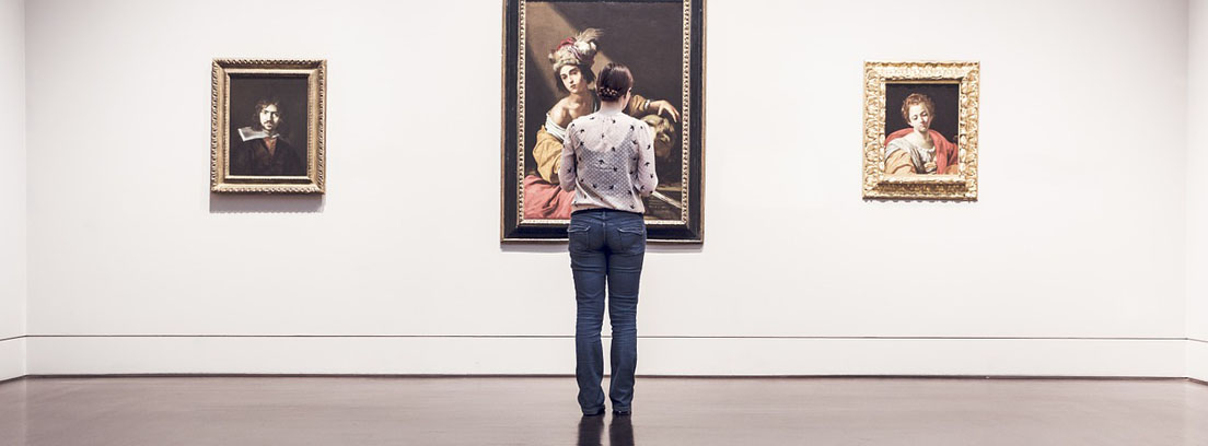 Mujer delante de tres cuadros colgados en pared blanca