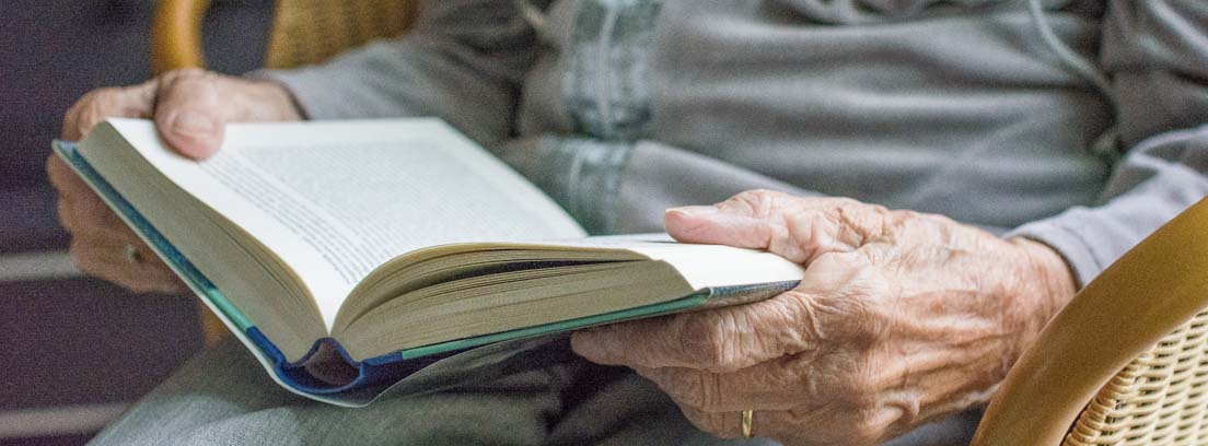 Manos de una persona mayor sosteniendo un libro en un centro de día para mayores