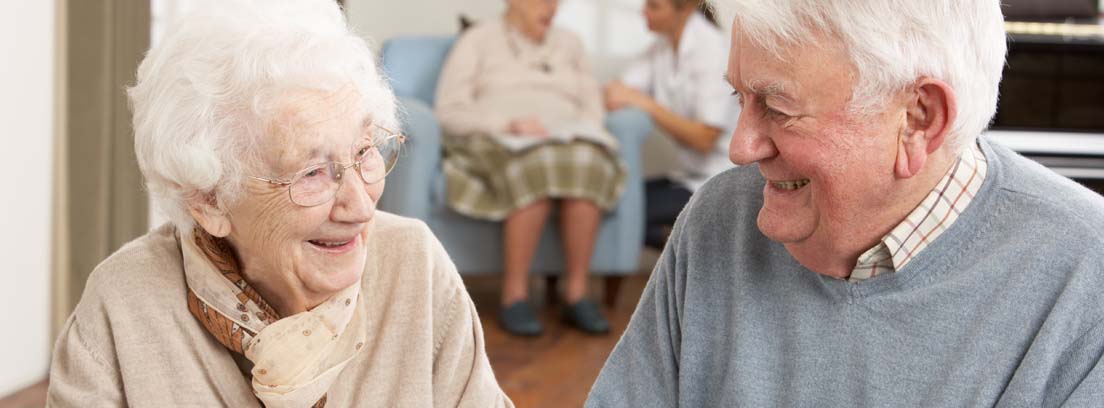 Hombre y mujer de avanzada edad sonrientes jugando al dominó en un centro de día para personas mayores