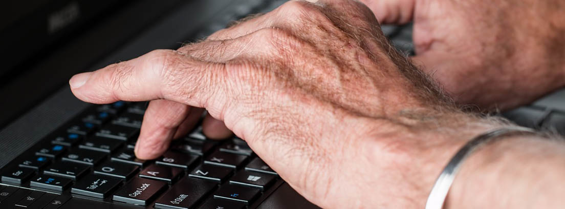 Manos de un jubilado sobre el teclado de un ordenador para buscar un club de jubilados