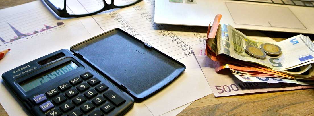 Calculadora sobre papeles junto a portátil y dinero