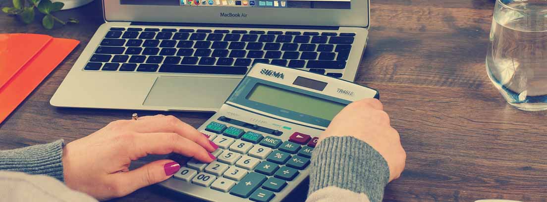 Mujer con una calculadora frente a un programa de contabilidad