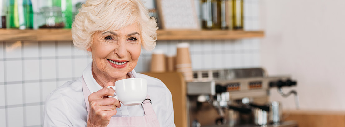 Mujer sonriente tomando una taza de café en su negocio disfrutando de una jubilación compatible con trabajo autónomo