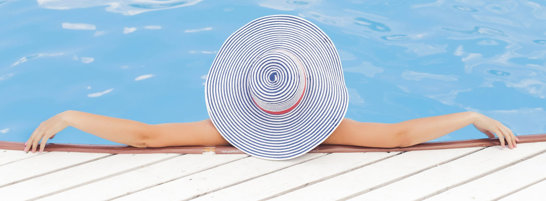 Mujer de espaldas con pamela metida en una piscina