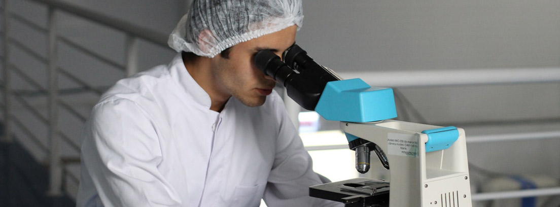 Investigador con bata y gorro blanco mirando por un microscopio
