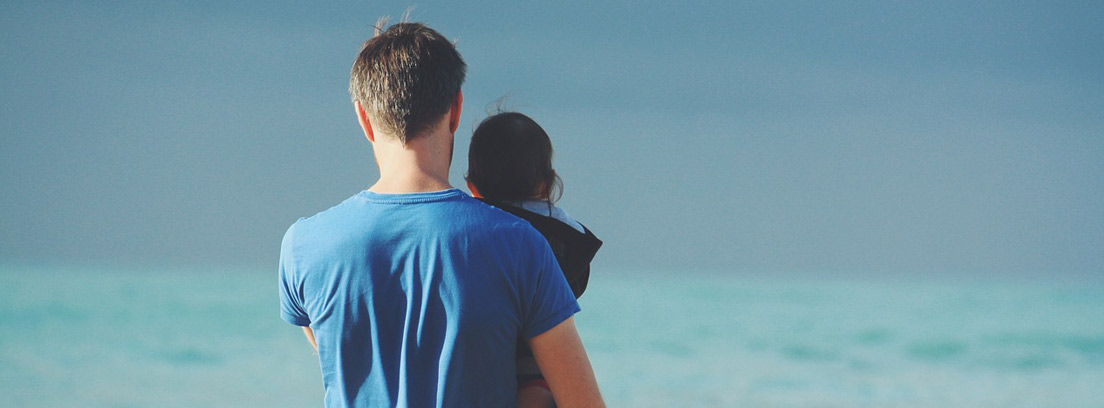 Hombre de espaldas con un niño en brazos en una playa