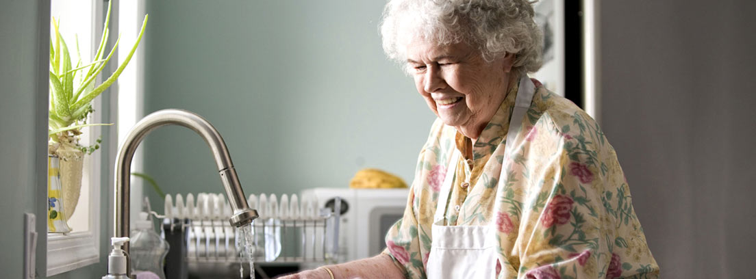 Mujer mayor lavando zanahorias en una cocina