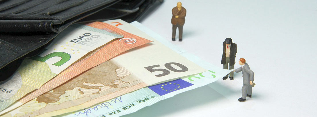 Pequeños muñecos al lado de billetes de euro saliendo de una cartera