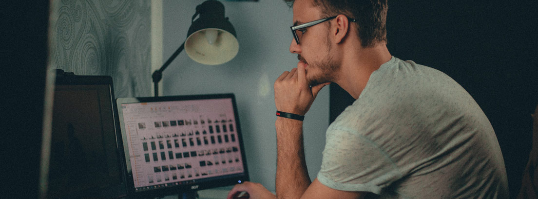 Hombre con gafas y manos sobre la barbilla mira ordenador