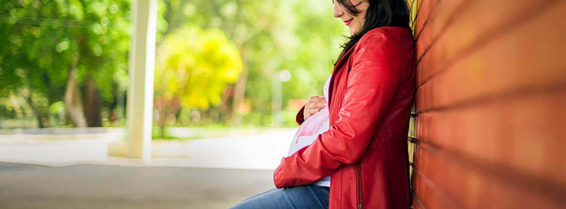 Mujer embaraza sentada en un banco sosteniendo su tripa