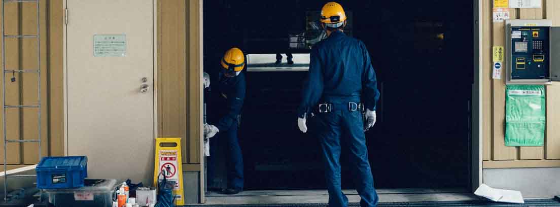 Operarios con monos azules y cascos amarillos trabajando en una puerta