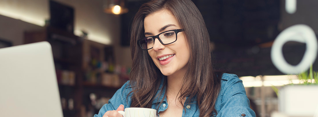 Mujer con una taza de café mirando un ordenador