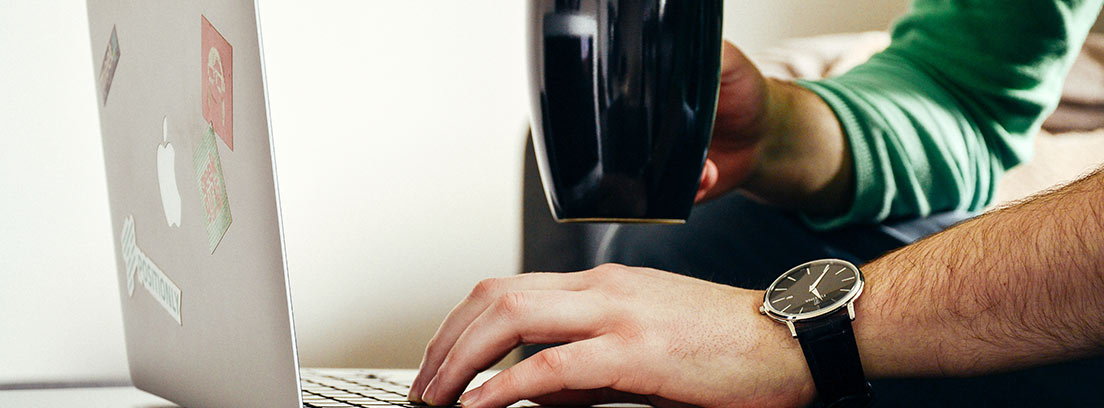 Hombre con una mano sujetando una taza y otra mano sobre un ordenador
