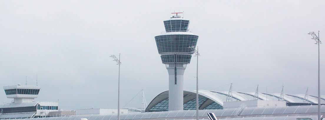 Varios aviones parados en el aeropuerto con torre de control al fondo
