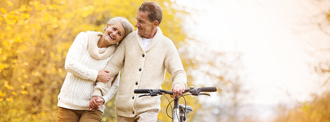 Hombre y mujer mayores con una bici paseando por un paisaje otoñal