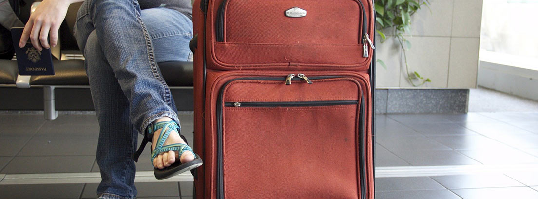 Mujer sentada junto a su maleta sosteniendo un pasaporte