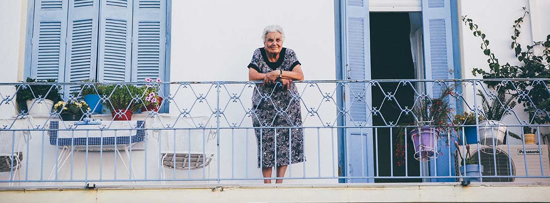 Mujer con pelo blanco apoya sus manos sobre la barandilla de la terraza de una casa