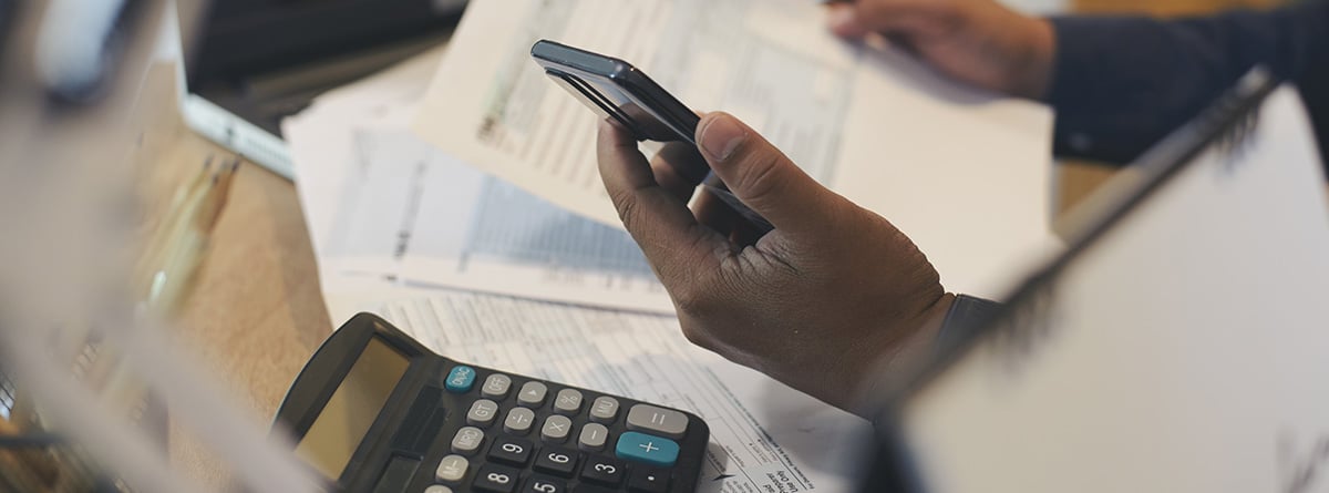 Cambiar la declaración de la renta: mano sosteniendo un móvil encima de una mesa con papeles y una calculadora