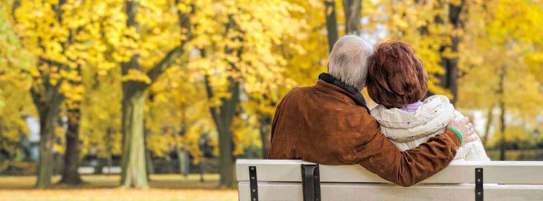 Hombre y mujer mayores sentados en un banco en un parque otoñal
