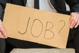 Hombre con traje sujetando un cartel en el que puede leerse: “Job?”