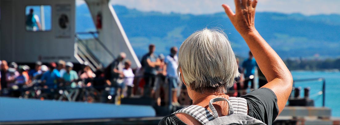Mujer mayor saludando a un barco lleno de gente