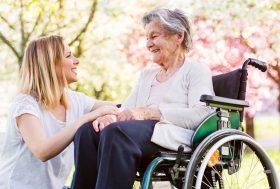 Mujer joven sonriendo a una mujer mayor sentada en una silla de ruedas