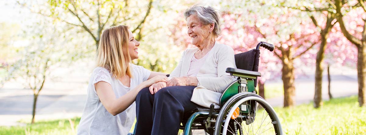 Mujer joven sonriendo a una mujer mayor sentada en una silla de ruedas