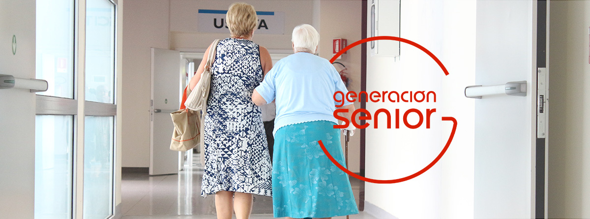 Mujer de la mano con otra mujer mayor caminando por el pasillo de un centro médico