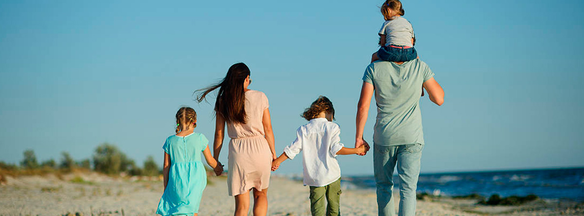 Dos adultos y tres niños caminando de espaldas por la playa