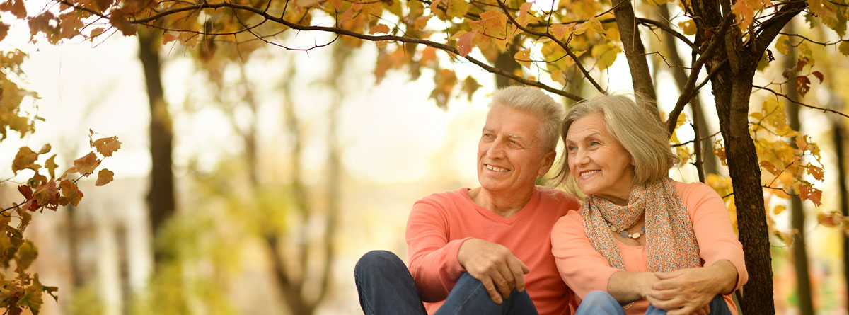 Hombre y mujer mayores sonrientes sentados en un campo otoñal