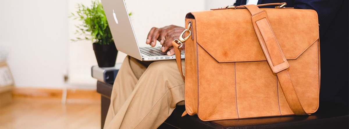 Empresario sentado utilizando su portátil junto a su cartera, como símbolo de buen inversor y exitoso