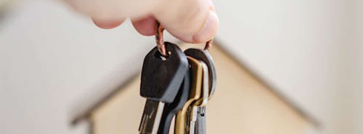 Una mano muestra un llavero con llaves con una casa de fondo.