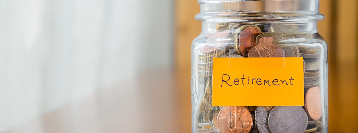 Un bote de cristal con cartel amarillo “Retirement” y monedas dentro.