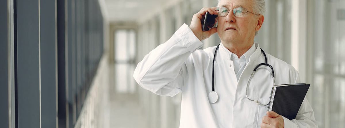  Un médico con gafas habla por teléfono en un pasillo de hospital.
