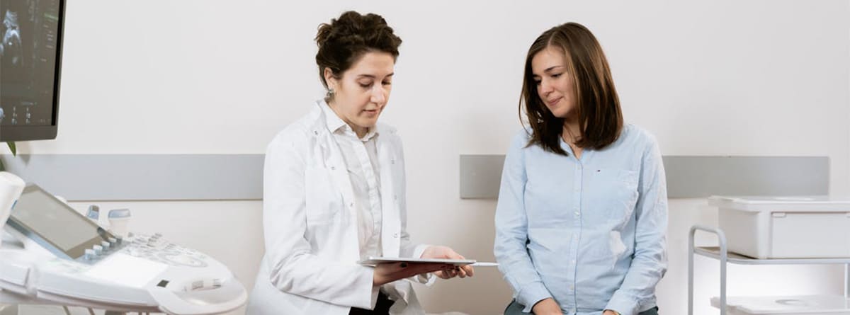 Una mujer y su médico consultan una documentación sentadas en una camilla.