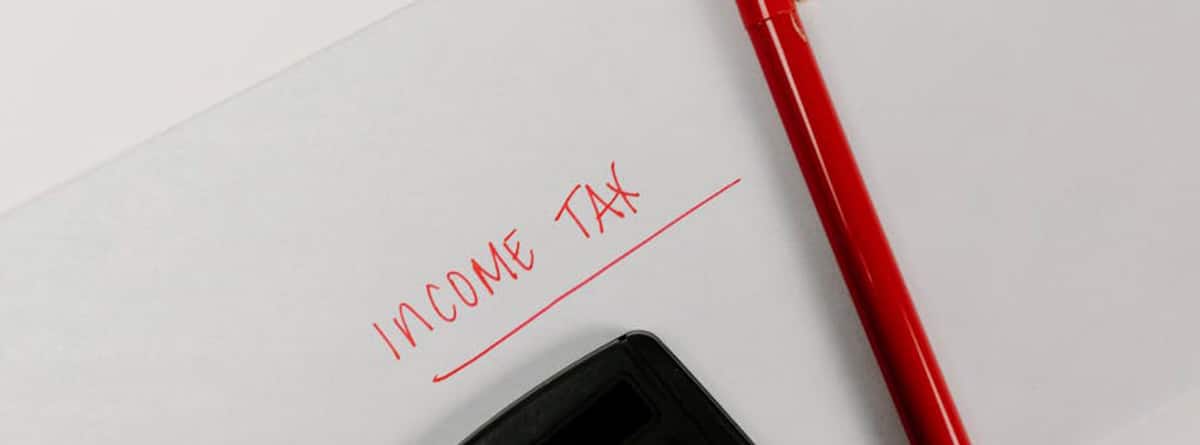 Calculadora y bolígrafo rojo con las palabras “Income tax” escritas en un papel.