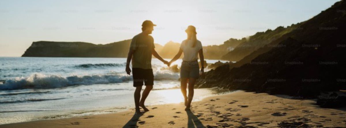 Una pareja pasea de la mano por una playa.